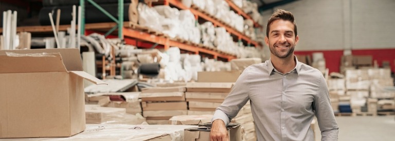 Manager glimlachend terwijl hij tegen de voorraad leunt in een groot magazijn